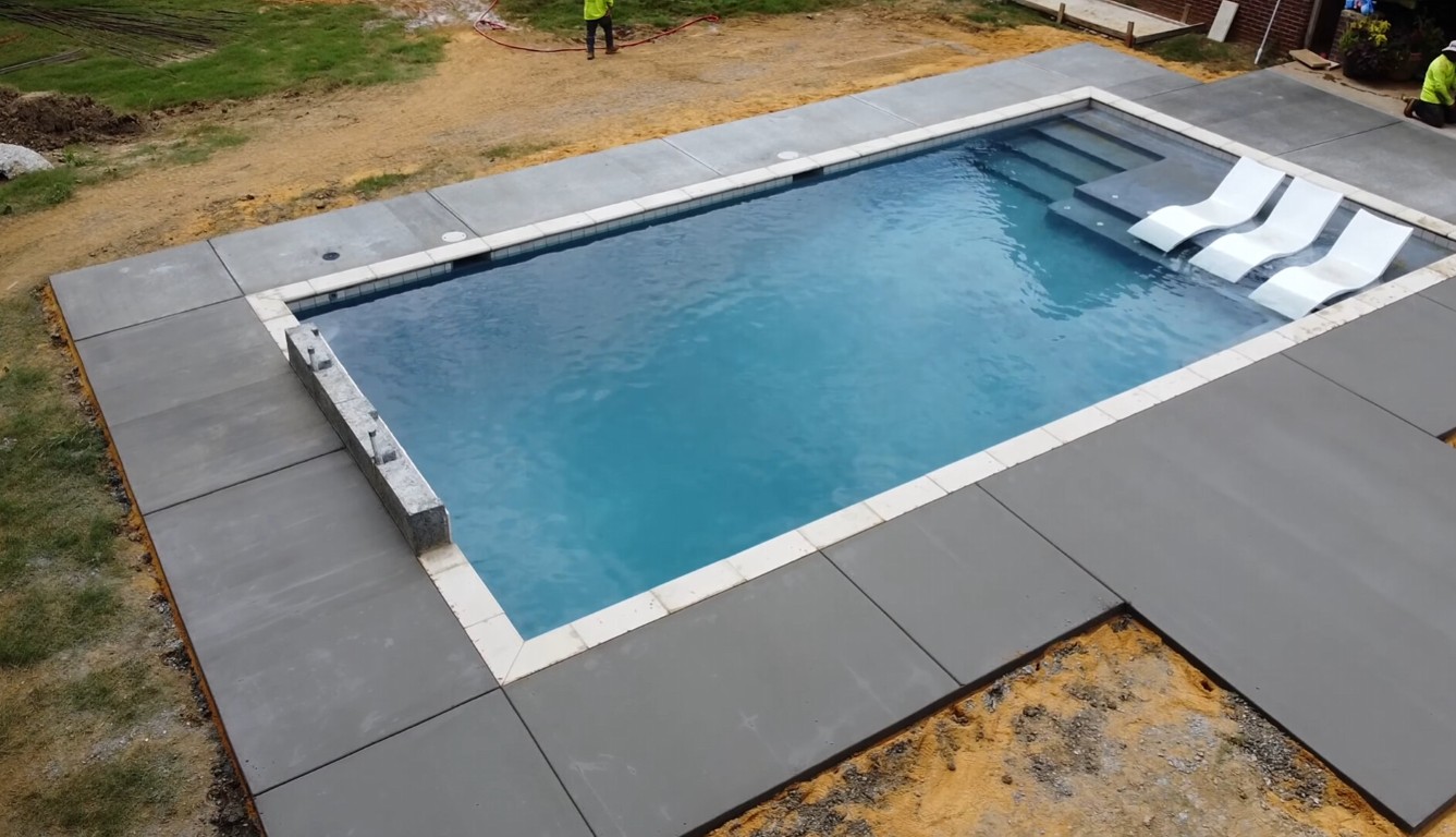 Modern concrete pool deck with steps surrounding residential swimming pool